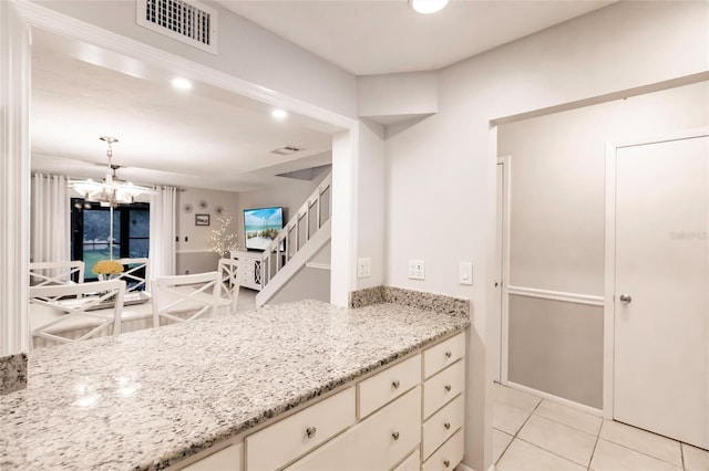 kitchen with light tile patterned flooring, cream cabinets, decorative light fixtures, a notable chandelier, and light stone countertops