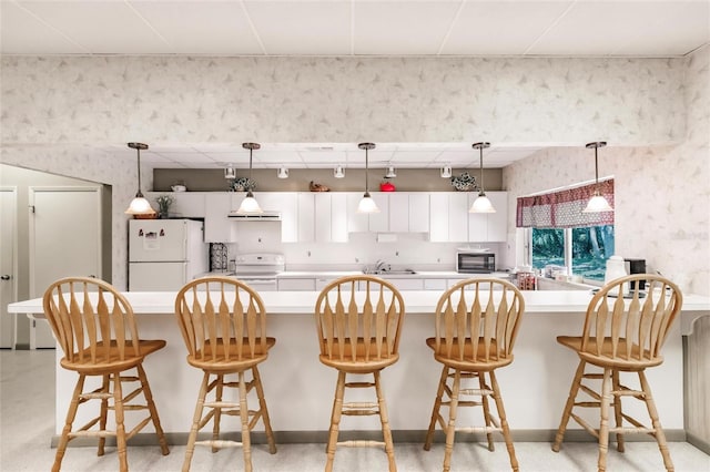 kitchen with white appliances, white cabinets, sink, and a breakfast bar