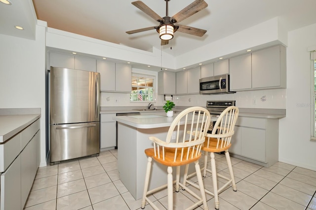 kitchen featuring a kitchen island, tasteful backsplash, a breakfast bar area, appliances with stainless steel finishes, and light tile patterned floors