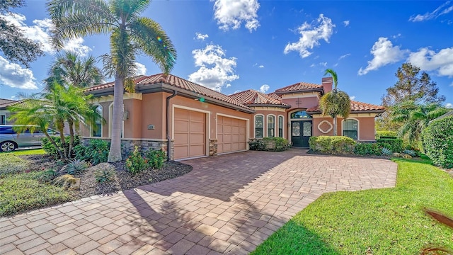 mediterranean / spanish home with a tiled roof, a chimney, decorative driveway, an attached garage, and stucco siding