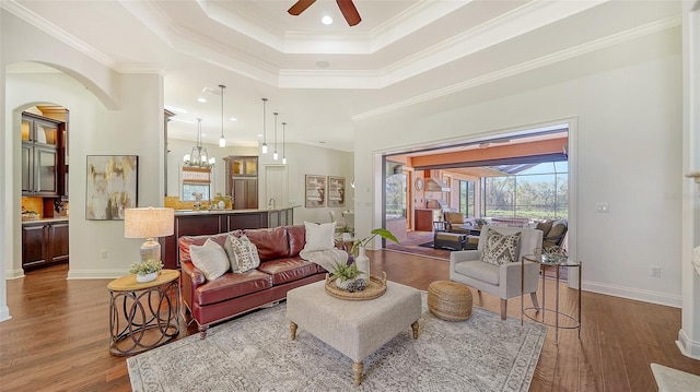 living area with a raised ceiling, ceiling fan, ornamental molding, and wood finished floors