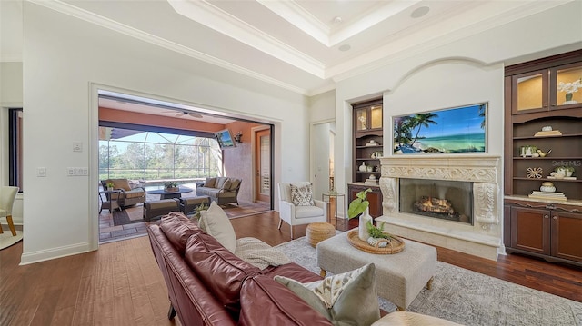 living room featuring crown molding, dark wood-style flooring, built in features, a sunroom, and a tray ceiling