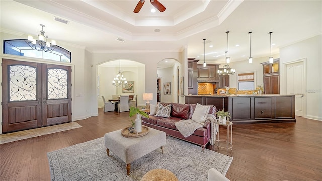 living area featuring a raised ceiling, arched walkways, dark wood finished floors, ceiling fan with notable chandelier, and visible vents