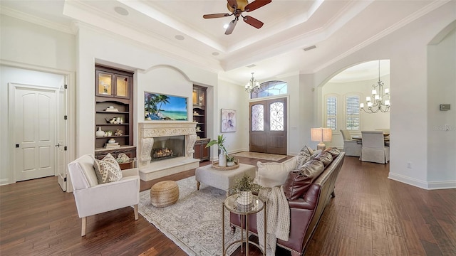 living area with dark wood-style flooring, a high end fireplace, a raised ceiling, arched walkways, and ceiling fan with notable chandelier