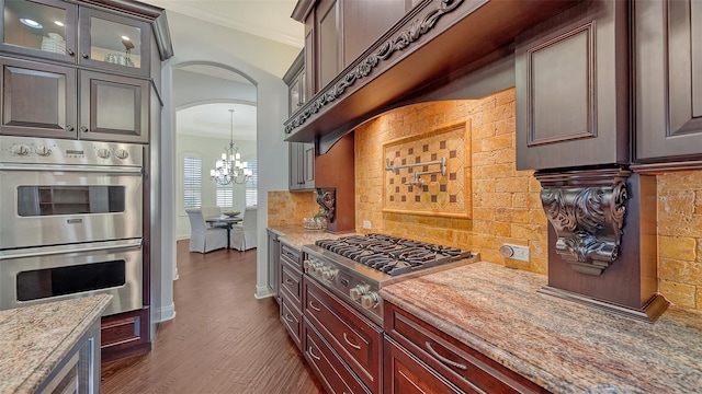 kitchen featuring appliances with stainless steel finishes, arched walkways, a chandelier, decorative backsplash, and dark wood-style floors