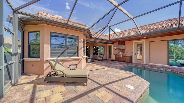 pool with glass enclosure, an outdoor kitchen, and a patio