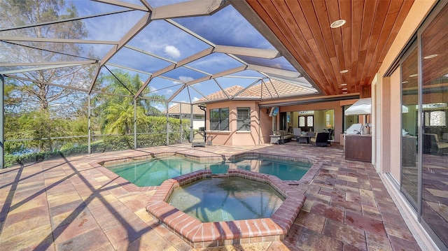 view of swimming pool with glass enclosure, a patio area, a pool with connected hot tub, and an outdoor kitchen