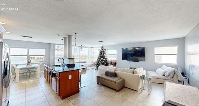 kitchen with stainless steel fridge, a center island with sink, a healthy amount of sunlight, pendant lighting, and sink