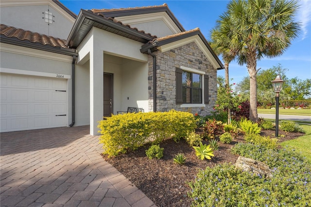 view of front of house with a garage, stone siding, a tile roof, and stucco siding