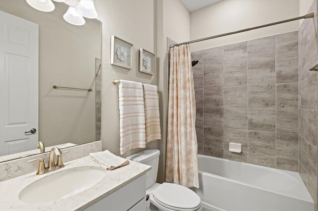 full bath with a textured wall, shower / bath combination with curtain, vanity, and toilet