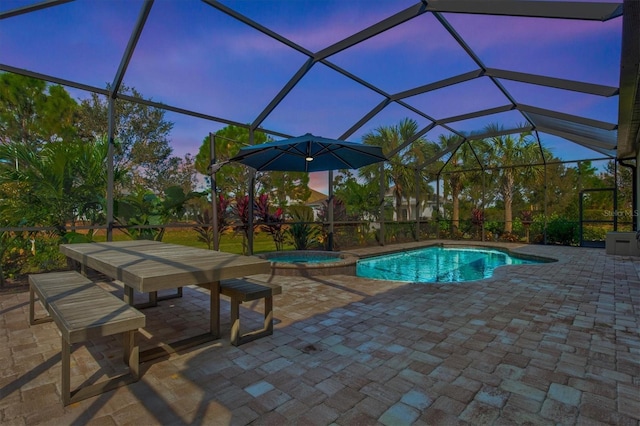 pool at dusk with a pool with connected hot tub, a patio, and a lanai