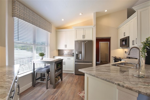 kitchen featuring stainless steel appliances, light stone countertops, backsplash, white cabinets, and lofted ceiling