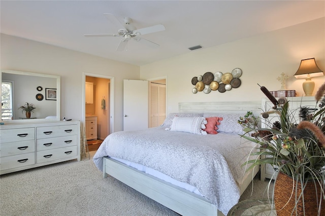 bedroom with ceiling fan, light colored carpet, a closet, and ensuite bathroom