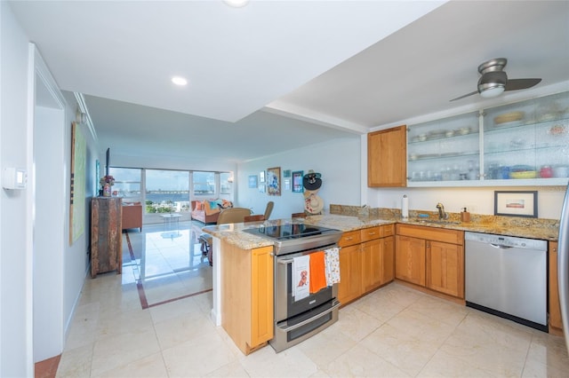 kitchen with appliances with stainless steel finishes, sink, a wall of windows, kitchen peninsula, and light stone countertops