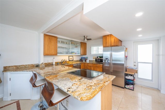 kitchen with sink, a breakfast bar, appliances with stainless steel finishes, light stone counters, and kitchen peninsula