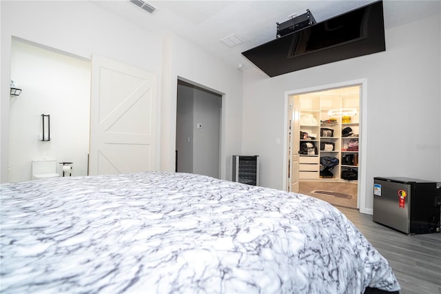 bedroom featuring a spacious closet, hardwood / wood-style flooring, a closet, and stainless steel fridge