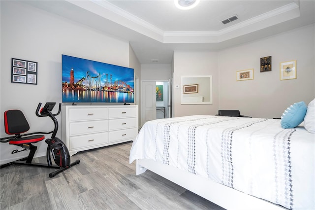 bedroom featuring crown molding, a raised ceiling, and light wood-type flooring