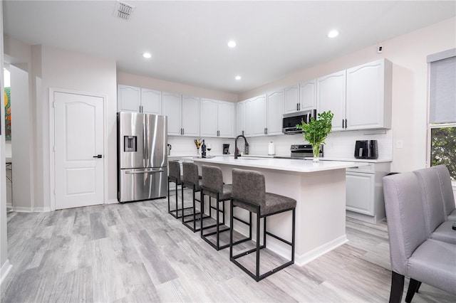 kitchen featuring appliances with stainless steel finishes, an island with sink, a breakfast bar, white cabinetry, and light hardwood / wood-style flooring