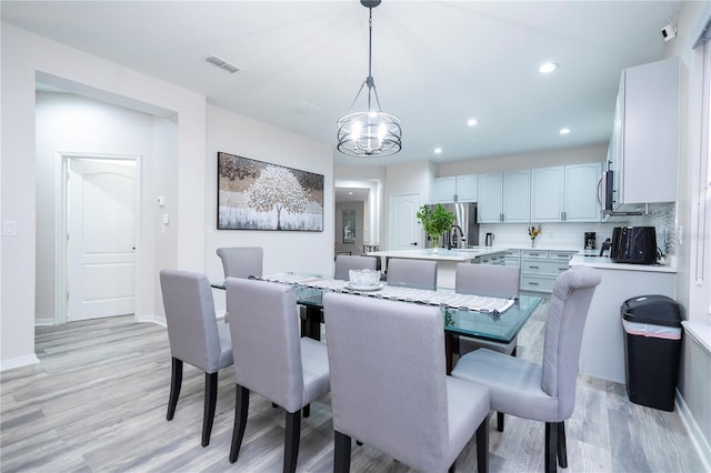 dining area with sink, light hardwood / wood-style flooring, and a notable chandelier