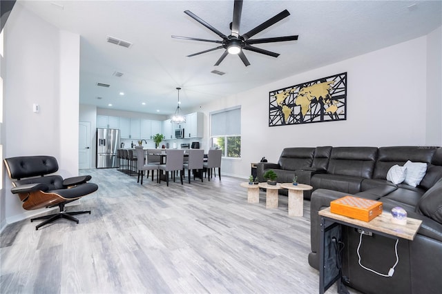 living room featuring light wood-type flooring and ceiling fan with notable chandelier