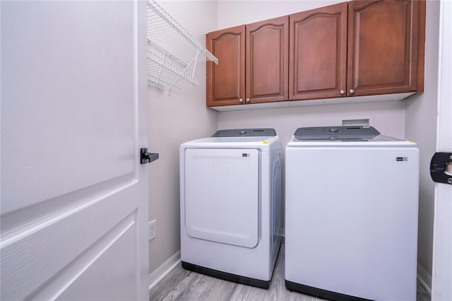 washroom featuring baseboards, light wood-style flooring, independent washer and dryer, and cabinet space