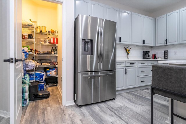 kitchen with decorative backsplash, light wood-style floors, baseboards, stainless steel refrigerator with ice dispenser, and light countertops