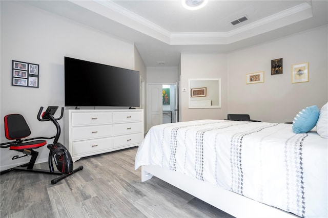 bedroom with visible vents, light wood-style floors, crown molding, and a tray ceiling
