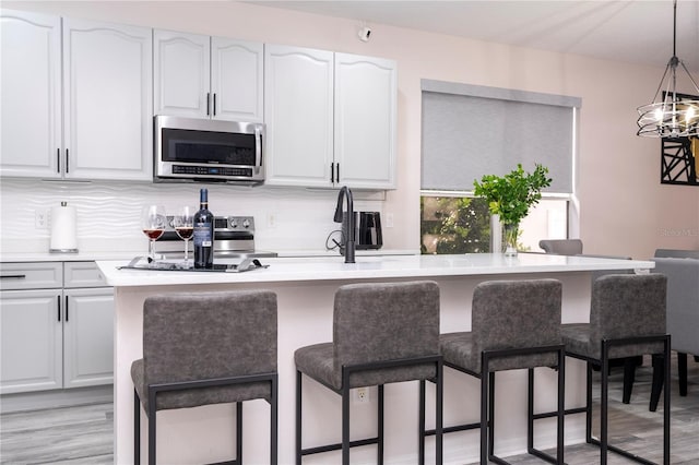kitchen with appliances with stainless steel finishes, a kitchen bar, white cabinetry, and decorative light fixtures