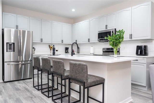 kitchen featuring decorative backsplash, a kitchen breakfast bar, a sink, light wood finished floors, and appliances with stainless steel finishes