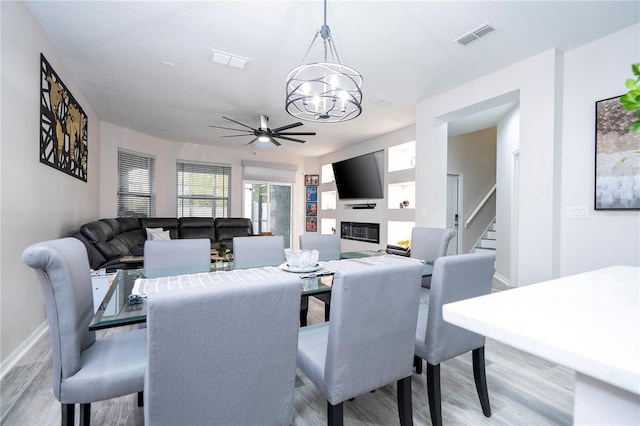 dining area with light wood-style floors, baseboards, a glass covered fireplace, and visible vents