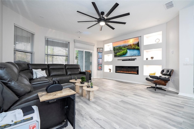 living area with ceiling fan, light wood-style floors, a glass covered fireplace, baseboards, and visible vents
