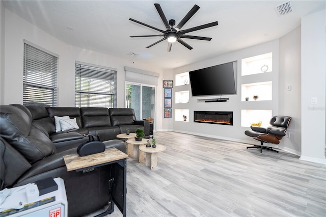 living room featuring visible vents, a glass covered fireplace, baseboards, light wood-type flooring, and a ceiling fan