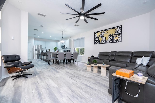 living area featuring a ceiling fan, baseboards, visible vents, and light wood finished floors