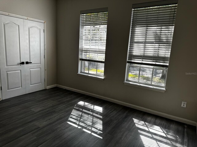unfurnished bedroom with baseboards, dark wood-style flooring, a closet, and multiple windows