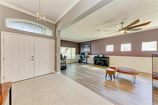 entrance foyer with ceiling fan with notable chandelier, light wood-type flooring, and ornamental molding