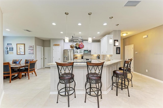 kitchen with white cabinetry, hanging light fixtures, stainless steel appliances, a kitchen breakfast bar, and light stone counters