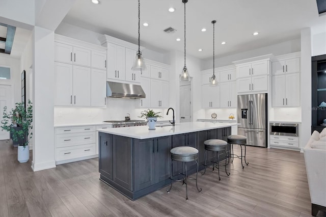 kitchen featuring appliances with stainless steel finishes, white cabinetry, a large island, decorative light fixtures, and range hood