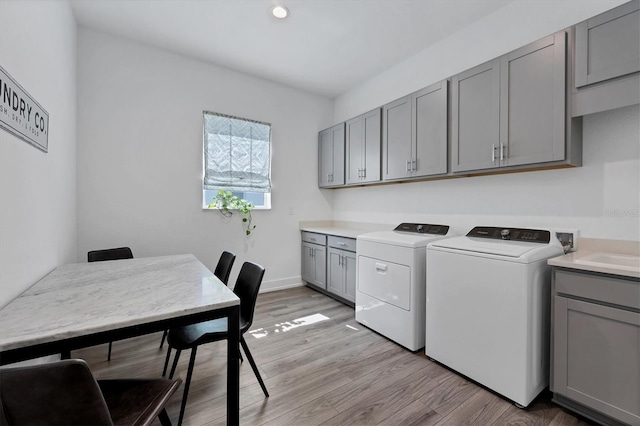 clothes washing area featuring washer and clothes dryer, light wood-type flooring, and cabinets