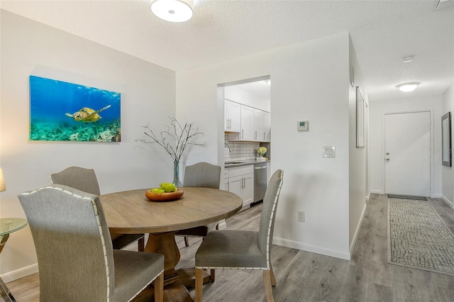 dining area featuring a textured ceiling, light wood-type flooring, and sink