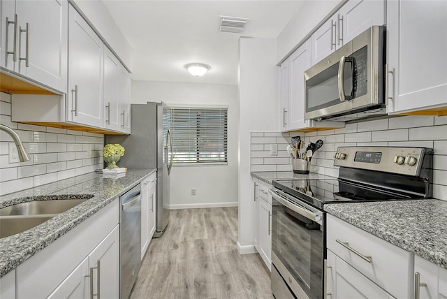 kitchen featuring backsplash, white cabinetry, light hardwood / wood-style flooring, and appliances with stainless steel finishes