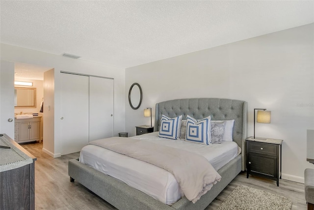 bedroom featuring ensuite bath, sink, wood-type flooring, a textured ceiling, and a closet