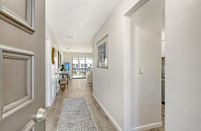 hall featuring light hardwood / wood-style flooring and a textured ceiling