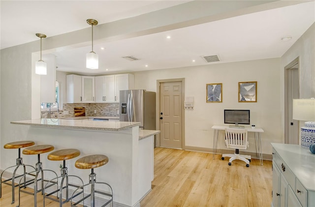 kitchen featuring tasteful backsplash, white cabinets, hanging light fixtures, stainless steel fridge with ice dispenser, and light stone countertops