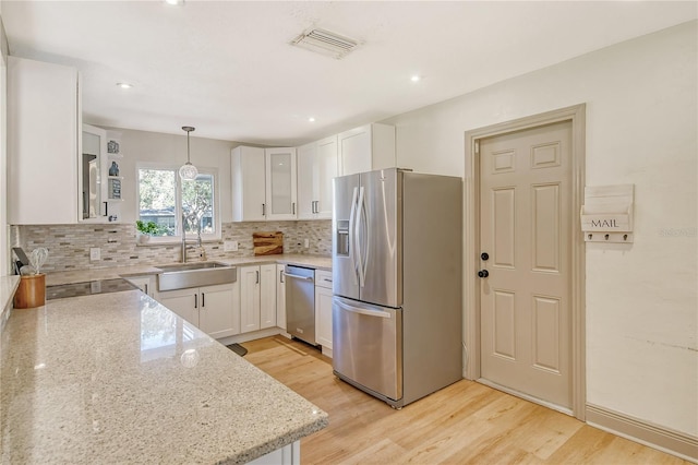 kitchen featuring appliances with stainless steel finishes, sink, white cabinets, hanging light fixtures, and light stone counters