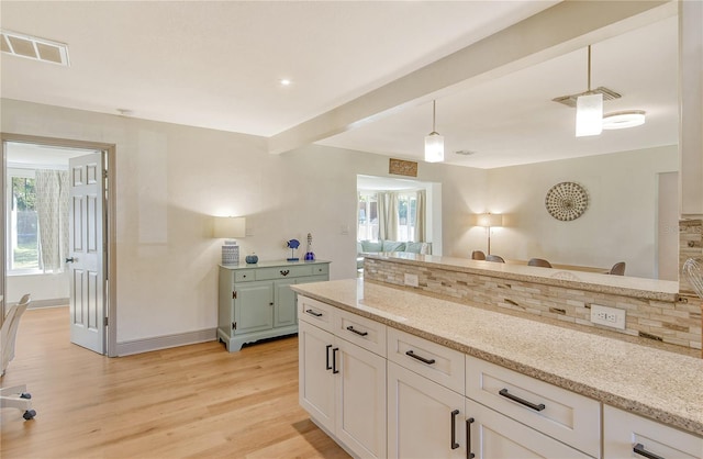 kitchen with hanging light fixtures, light stone countertops, white cabinets, and light wood-type flooring