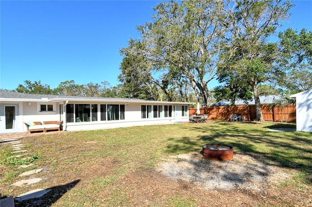 rear view of property with a sunroom, a lawn, and a fire pit