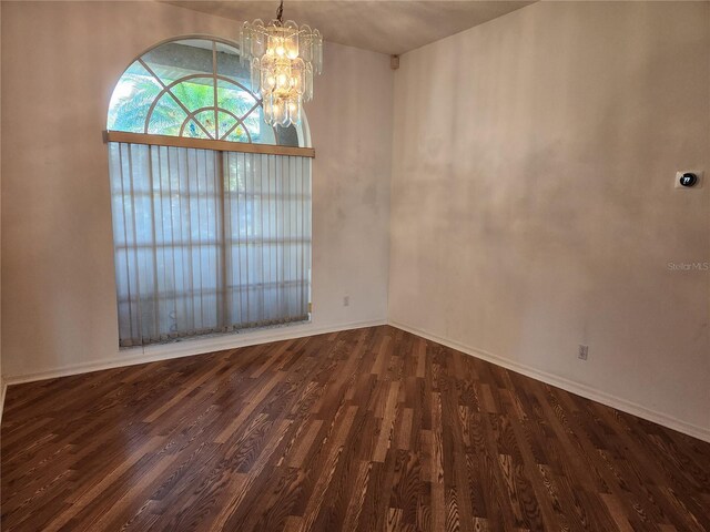 empty room with dark hardwood / wood-style floors and a chandelier