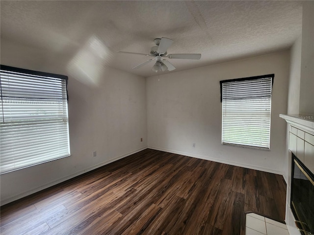 empty room with ceiling fan, dark hardwood / wood-style flooring, a textured ceiling, and a tile fireplace