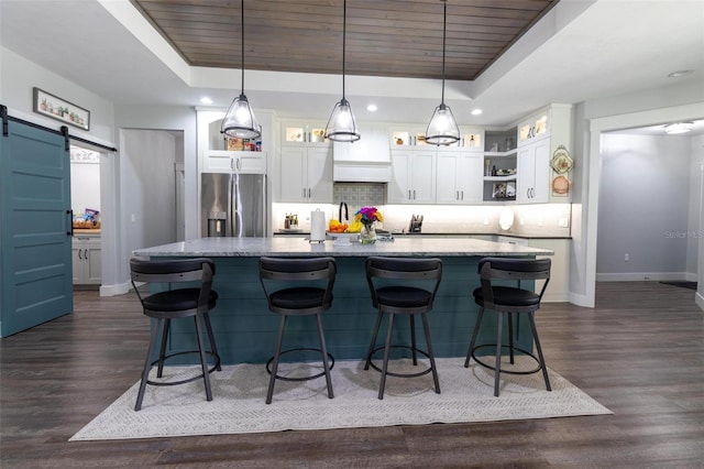 kitchen with white cabinets, a raised ceiling, a barn door, and stainless steel fridge