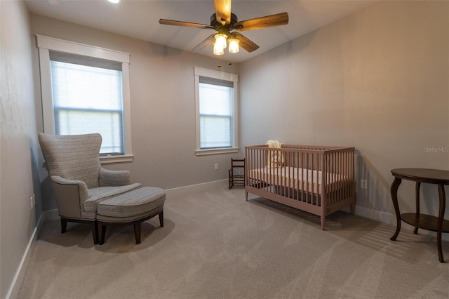 carpeted bedroom featuring a nursery area and ceiling fan